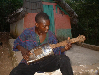 A Haitian boy plays a home-made guitar.  This photo was taken several years ago while in Haiti on a shoot.